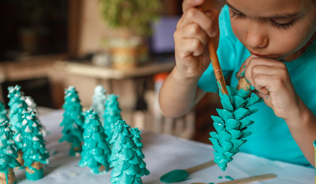 DIY craft gifts and Christmas decoration. Girl coloring cone as if it is pine tree, be green