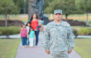 man in camo uniform stands in front of family